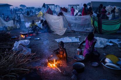 Un niño se calienta cerca de una hoguera mientras su madre prepara la cena en el campo de desplazados de Bentiu, en Sudán del Sur.