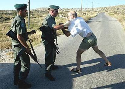 Dos policías de frontera israelíes tratan de impedir que un colono judío se aproxime a la colonia ilegal deshabitada en Gaza, que va a ser destruida.