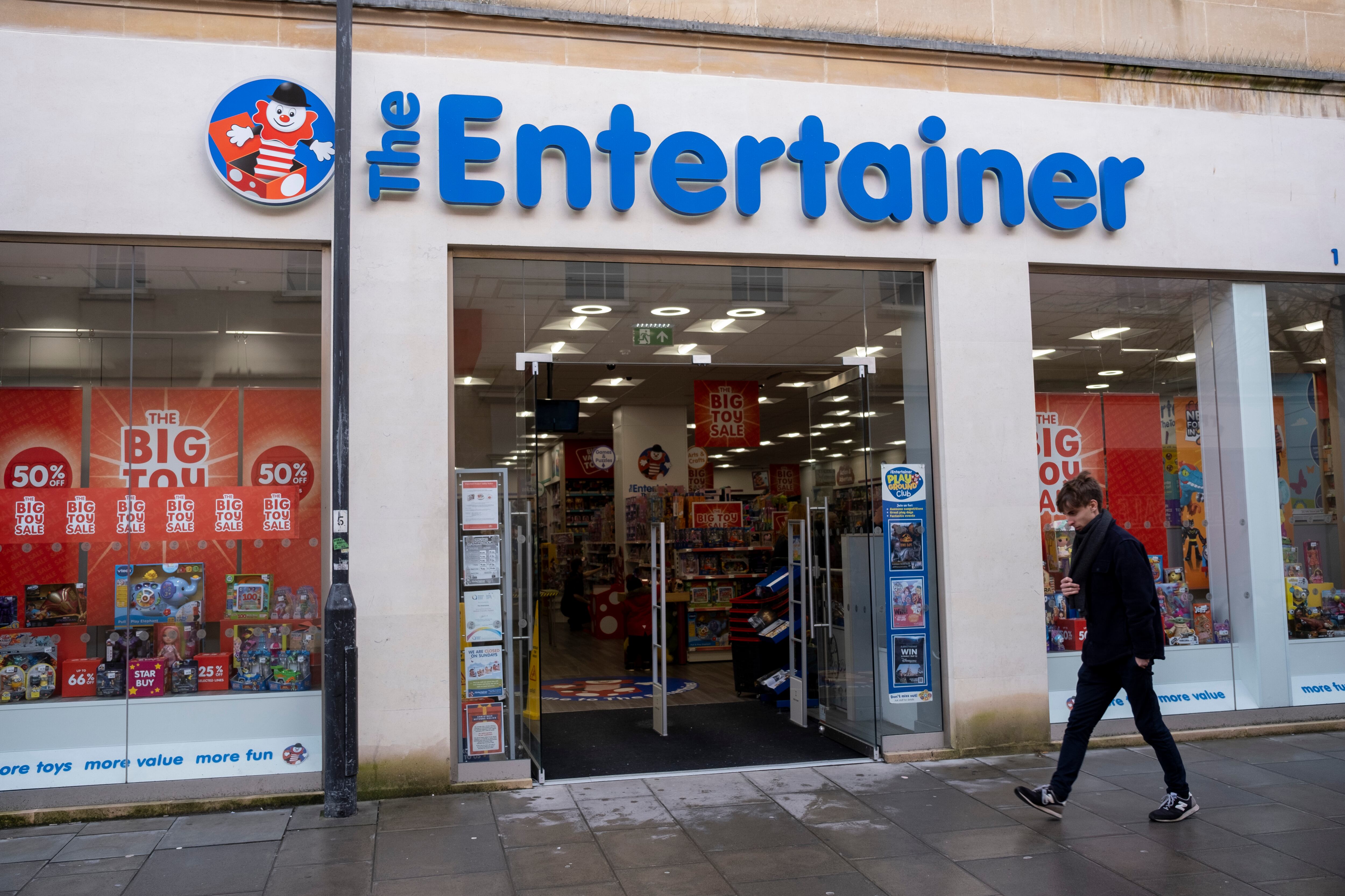 Person out and about in the city centre passes The Entertainer toy shop on 29th December 2022 in Bath, United Kingdom. Bath is a city in the county of Somerset, known for and named after its Roman-built baths, and Georgian architecture made from the local