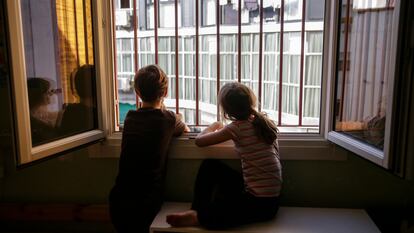 Dos hermanos miran por la ventana de su dormitorio durante el confinamiento en Madrid, el 13 de abril. 