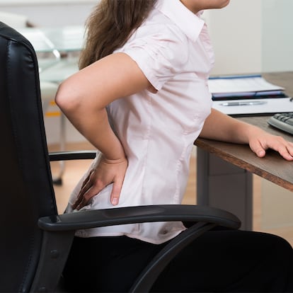 Una chica tocándose la espalda baja sentada en una silla de oficina.