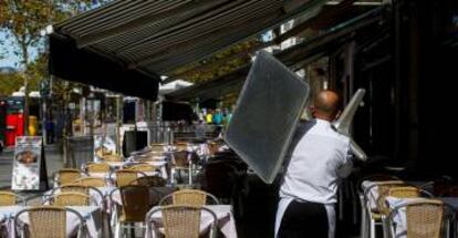 Un camarero recoge una mesa de una terraza de un restaurante del barrio de la Barceloneta de Barcelona.