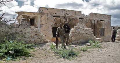 Milicianos hacen guardia frente a las ruinas de una casa, uno de ellos se apoya en los restos de un obús, agosto de 2011