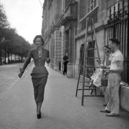 Laborers watch a well-dressed woman walking down the street in an undated image.