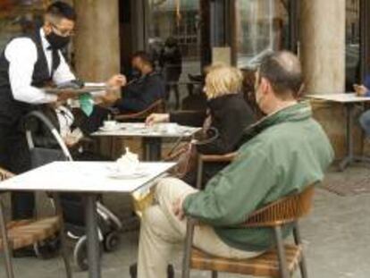 Un camarero atiende a varios clientes en la terraza de un bar.