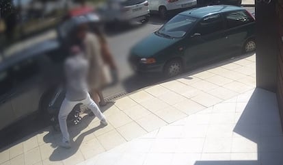 Uno de los ladrones de relojes, de espaldas, aborda a una vctima en el momento que ha dejado un carrito de beb junto a un coche y se dispone a meter en el maletero unas bolsas.