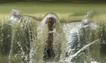 Un hombre se refresca bajo una pequeña cascada en el Jardín Inglés en Munich, Alemania.