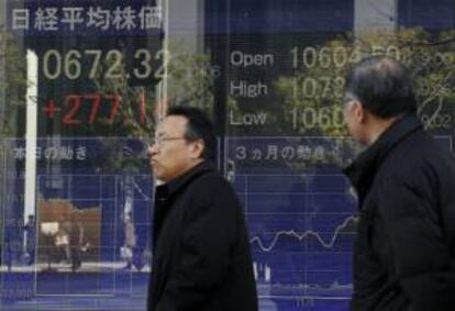 Dos hombres pasan por delante de un panel que muestra la evolocuón del índice Nikkei de la Bolsa de Tokio. El mercado de valores abrió hoy con una subida del 1,66 por ciento. EFE/Archivo