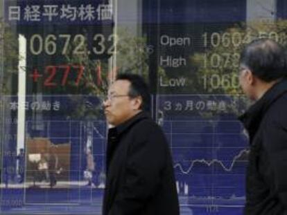 Dos hombres pasan por delante de un panel que muestra la evolocuón del índice Nikkei de la Bolsa de Tokio. El mercado de valores abrió hoy con una subida del 1,66 por ciento. EFE/Archivo