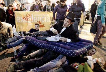 Un estudiante disfrazado de hombre rico se acuesta sobre un grupo de estudiantes durante la protesta en Madrid.