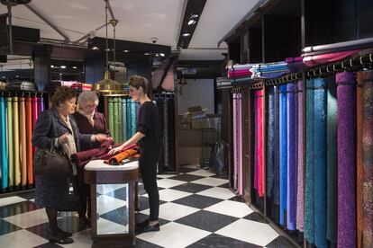 Una dependenta mostra teixits de diferents colors a dues clientes de la botiga.