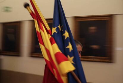 Un trabajador de la sede de la patronal catalana Fomento del Trabajo en Barcelona, coloca unas banderas de Cataluña, España y Europa.