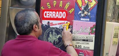 Un comerciante intenta quitar una pegatina de la huelga en un comercio de la calle Preciados de Madrid