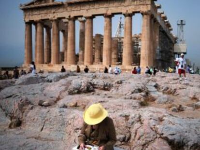 Una turista consulta su guía de viaje sentada junto al Partenón, en la Acrópolis de Atenas.