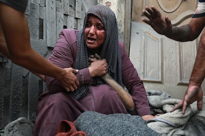 Una mujer palestina herida llora mientras sostiene la mano de su familiar muerto frente a su casa, tras los ataques aéreos israelíes dirigidos contra su barrio en la ciudad de Gaza, este lunes.