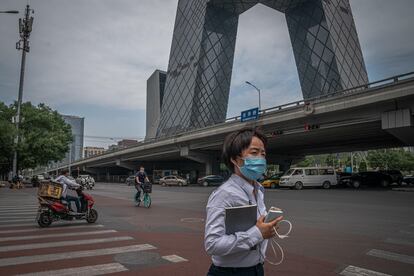 Una mujer con mascarilla pasea frente a la sede de la televisión estatal china, CCTV, uno de los edificios más emblemáticos de Pekín