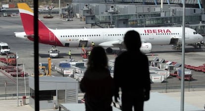 Dos personas miran un avión de Iberia desde la terminal 4 de Barajas.