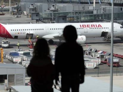 Dos personas miran un avi&oacute;n de Iberia desde la terminal 4 de Barajas. 