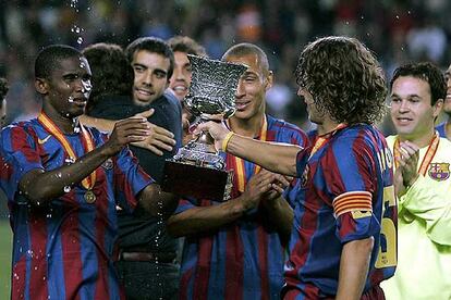 Puyol ofrece el trofeo de la Supercopa, el sexto que consigue el Barcelona, a su compañero Eto'o, mientras otros jugadores azulgrana se abrazan. El equipo de Rijkaard ganó 0-3 en la ida por lo que, pese a la derrota por 1-2 en el Camp Nou, han conseguido un nuevo título.