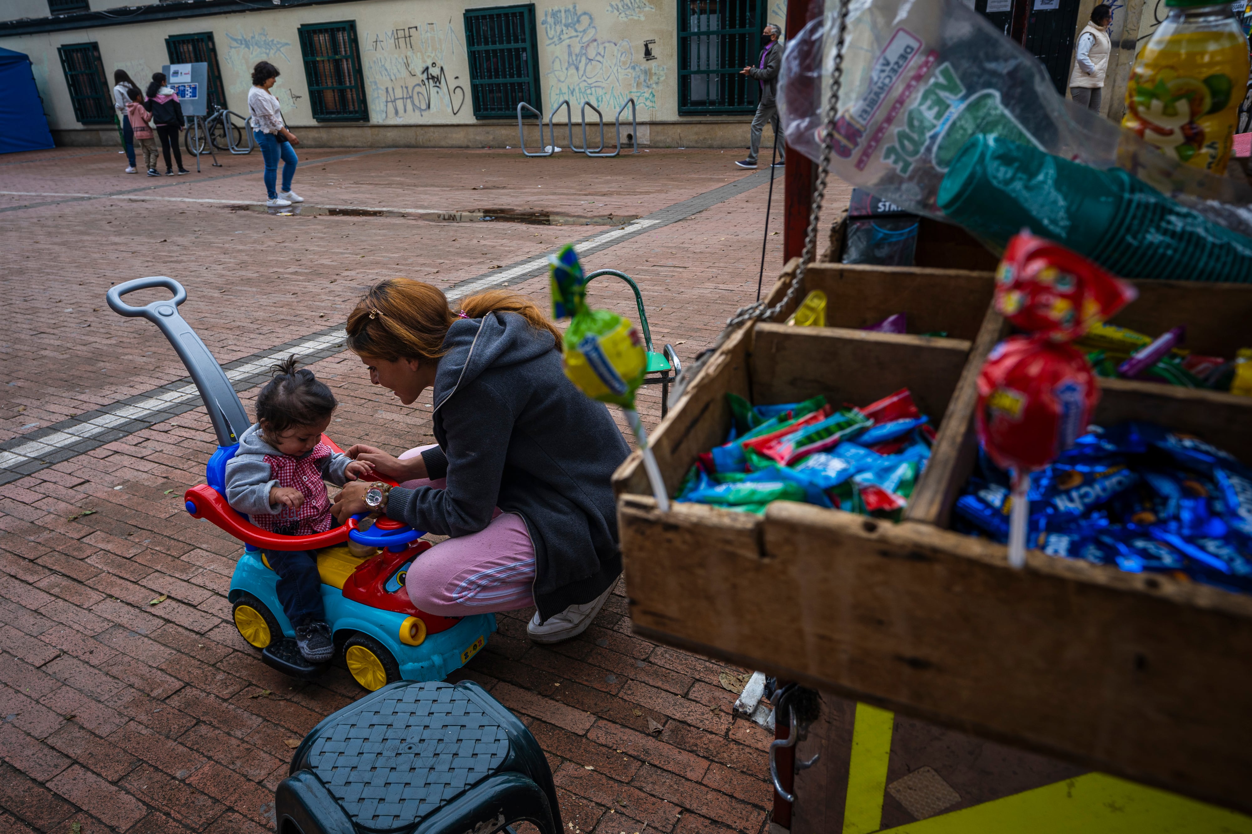 Kimberly juega con uno de sus hijos en su puesto ambulante al frente de una de las unidades móviles de las Manzanas del  Cuidado en la localidad de Fontibón, donde se realizan actividades educativas en Bogotá, Colombia el 21 de noviembre del 2022.