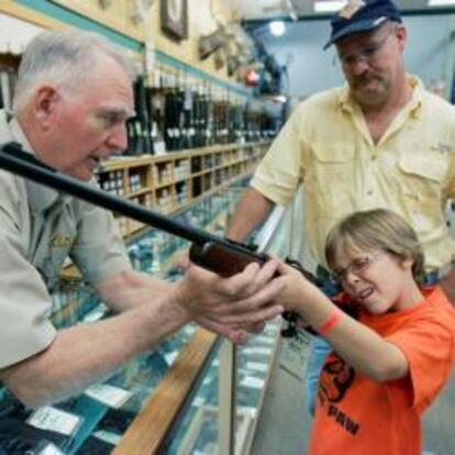 Un distribuidor de armas ayuda a un niño a sujetar un rifle en presencia de su padre en Fort Worth, Texas.