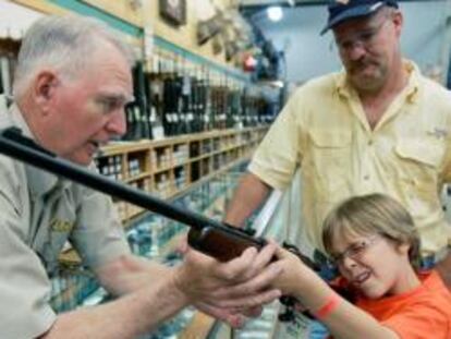 Un distribuidor de armas ayuda a un niño a sujetar un rifle en presencia de su padre en Fort Worth, Texas.