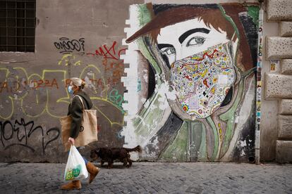 Una mujer con mascarilla pasea ante un mural en Roma.