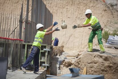 Dos obreros se pasan un botijo para beber mientras trabajan.