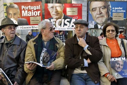 Seguidores de Aníbal Cavaco Silva leen sentados ante los carteles de tres de los seis aspirantes a la presidencia de Portugal mientras esperan en Lisboa la llegada del candidato conservador. Cavaco, que ha prometido acabar con la crisis económica, es el favorito para imponerse en la primera vuelta de las elecciones presidenciales que se celebran el domingo en Portugal.