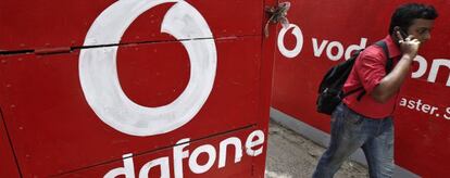 Un hombre habla con su m&oacute;vil al lado de un logotipo de Vodafone.