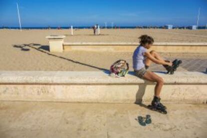 Una mujer se ajusta los patines en la playa de la Malvarrosa.