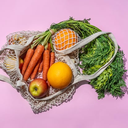 Reusable cotton mesh bag with fruit and vegetables on pink background. Zero Waste shopping concept.