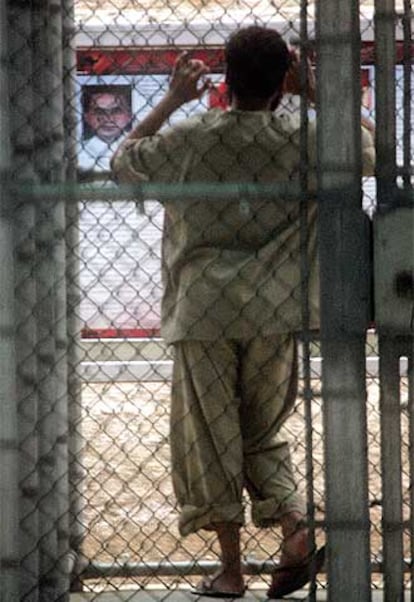 Un detenido en Guantánamo mira a través de una alambrada boletines informativos facilitados por los militares.