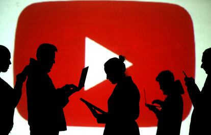 Varias personas revisan sus dispositivos electrónicos frente al logo de YouTube.
