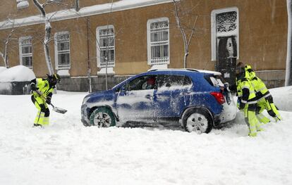 Varios bomberos tratan de sacar un coche atascado por la nieve.