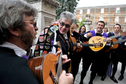 El premio Cervantes 2009 escucha a los miembros de la tuna de la Universidad de Alcalá, con una de sus capas puesta.