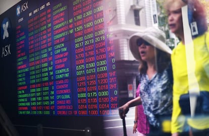 Reflejo de dos personas en un cristal mientras un monitor informa de los valores del mercado bursátil australiano ASX, en Sídney (Australia)