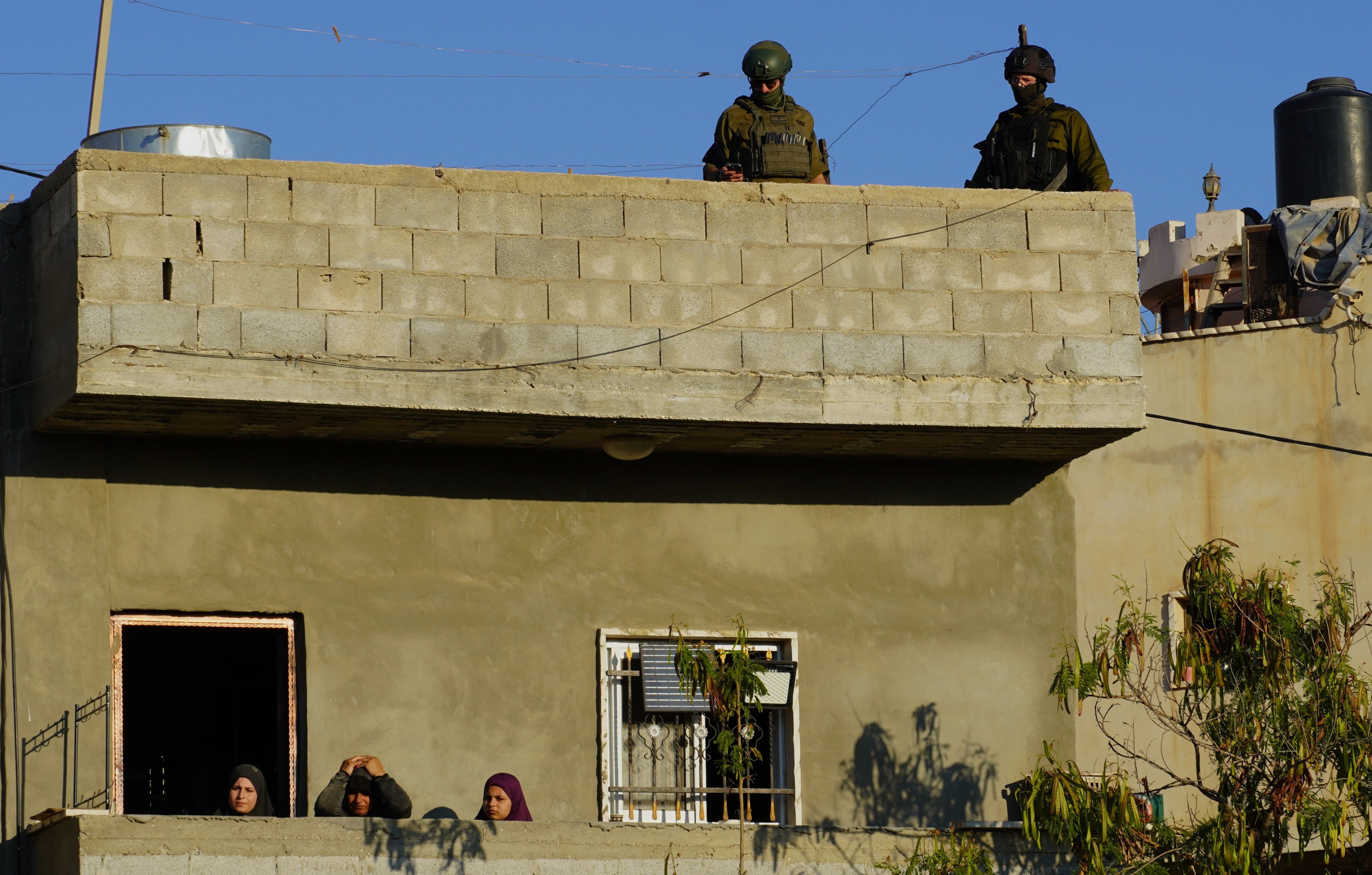 Soldados israelíes vigilan desde la azotea de una casa palestina el rezo, que siguen desde un balcón mujeres palestinas.
