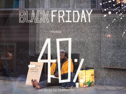 Una persona sin hogar pide limosna frente a un cartel de descuentos días previos al ‘Black Friday’ en Madrid.