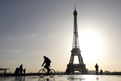 Un ciclista y varios paseantes, frente a la torre Eiffel de París.