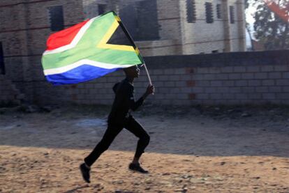Un aficionado corre con la bandera de Sudáfrica en las inmediaciones del estadio Soccer City, en Johanesburgo, escenario del partido inaugural y de la final.