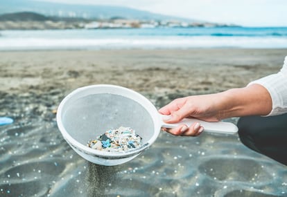 Una mujer limpiando microplásticos de la arena en la playa.