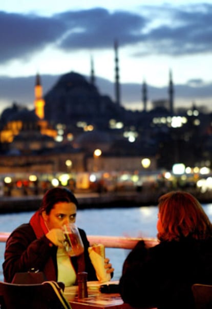 Dos jvenes en una terraza cerca del puente de Galata, con la silueta de la mezquita de Sulemaniye al fondo.