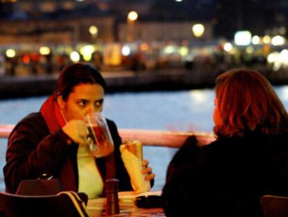 Dos jóvenes en una terraza cerca del puente de Galata, con la silueta de la mezquita de Sulemaniye al fondo.