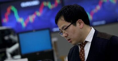 Un corredor de bolsa trabaja junto a monitores que ofrecen la información bursátil en Seúl (Corea).