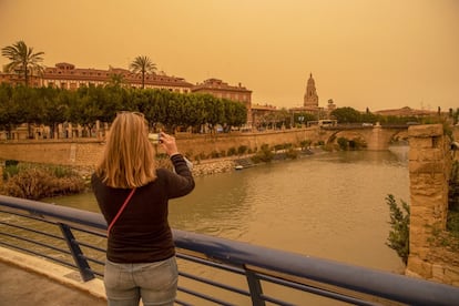 Una mujer hace una fotografía con su móvil en el centro de Murcia, afectada por el episodio de calima que ha teñido de naranja los cielos y las calles de la ciudad.