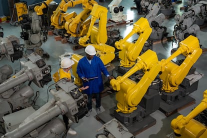 Dos operarios supervisa el proceso de fabricación y desarrollo de brazos robóticos de automatización personalizada, en un centro de distribución de robots industriales.
