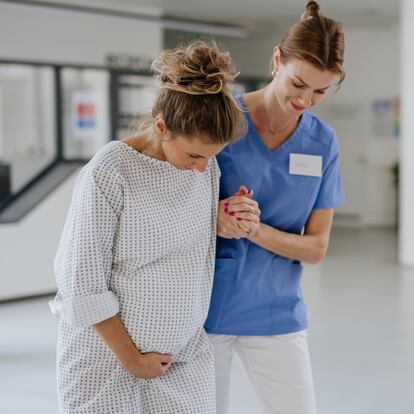 Nurse helping pregnant woman with painful labour contractions in the hospital hall. Woman in labor, dressed in hospital gown doing breathing exercises, deep breathing to relieve pain. Woman giving birth at the maternity hospital, ward.