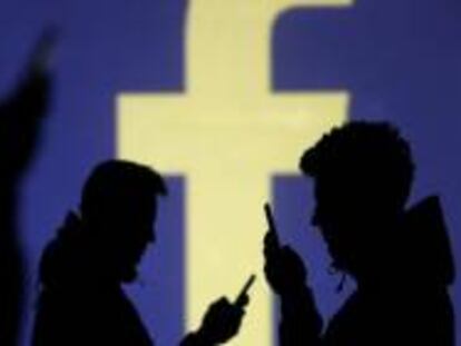 Varias personas consultan su móvil frente a un logo de Facebook.