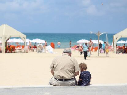 Un abuelo se sienta con su nieta en el poyete de un paseo marítimo.